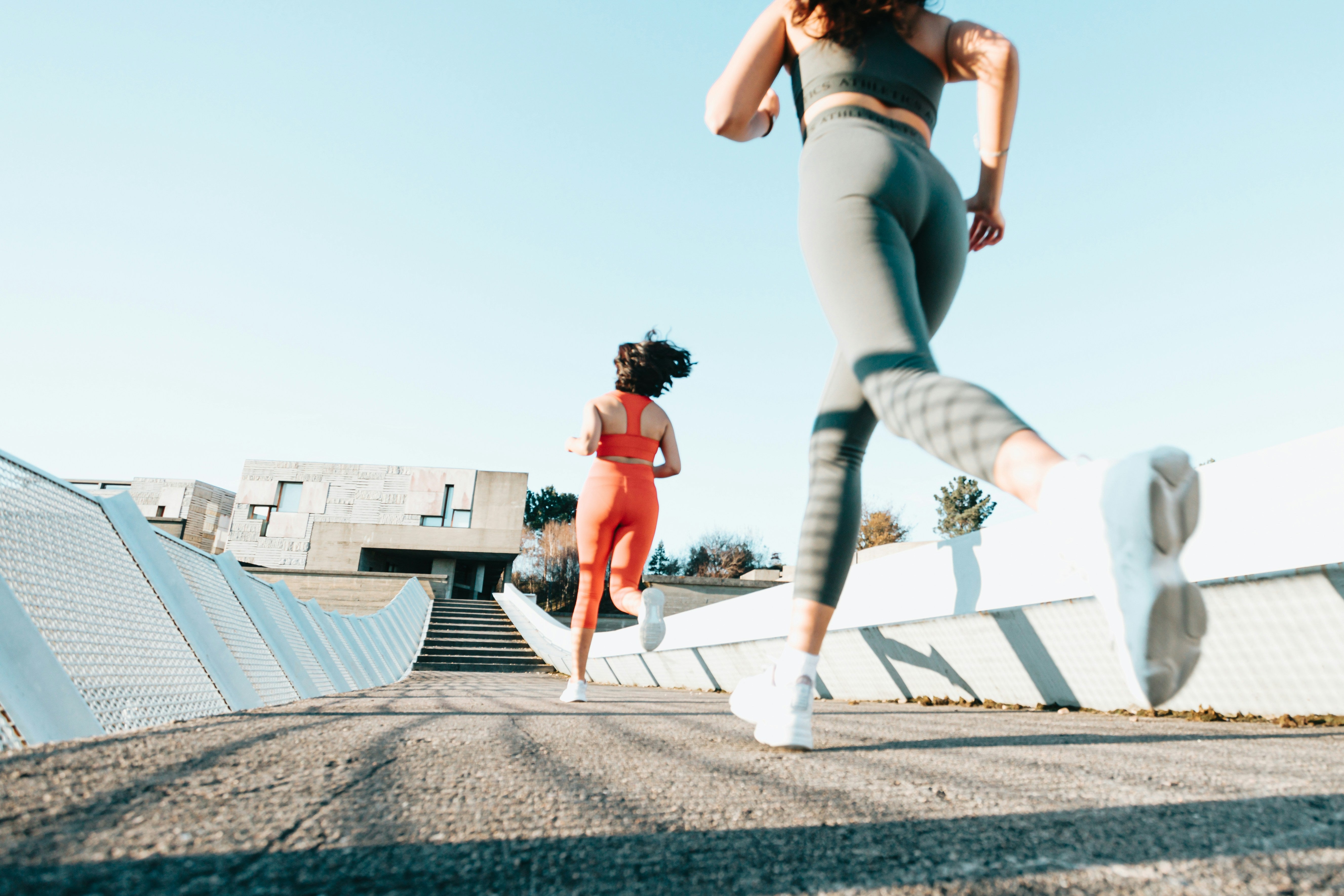 Two women running on a path with modern architectural elements in the background