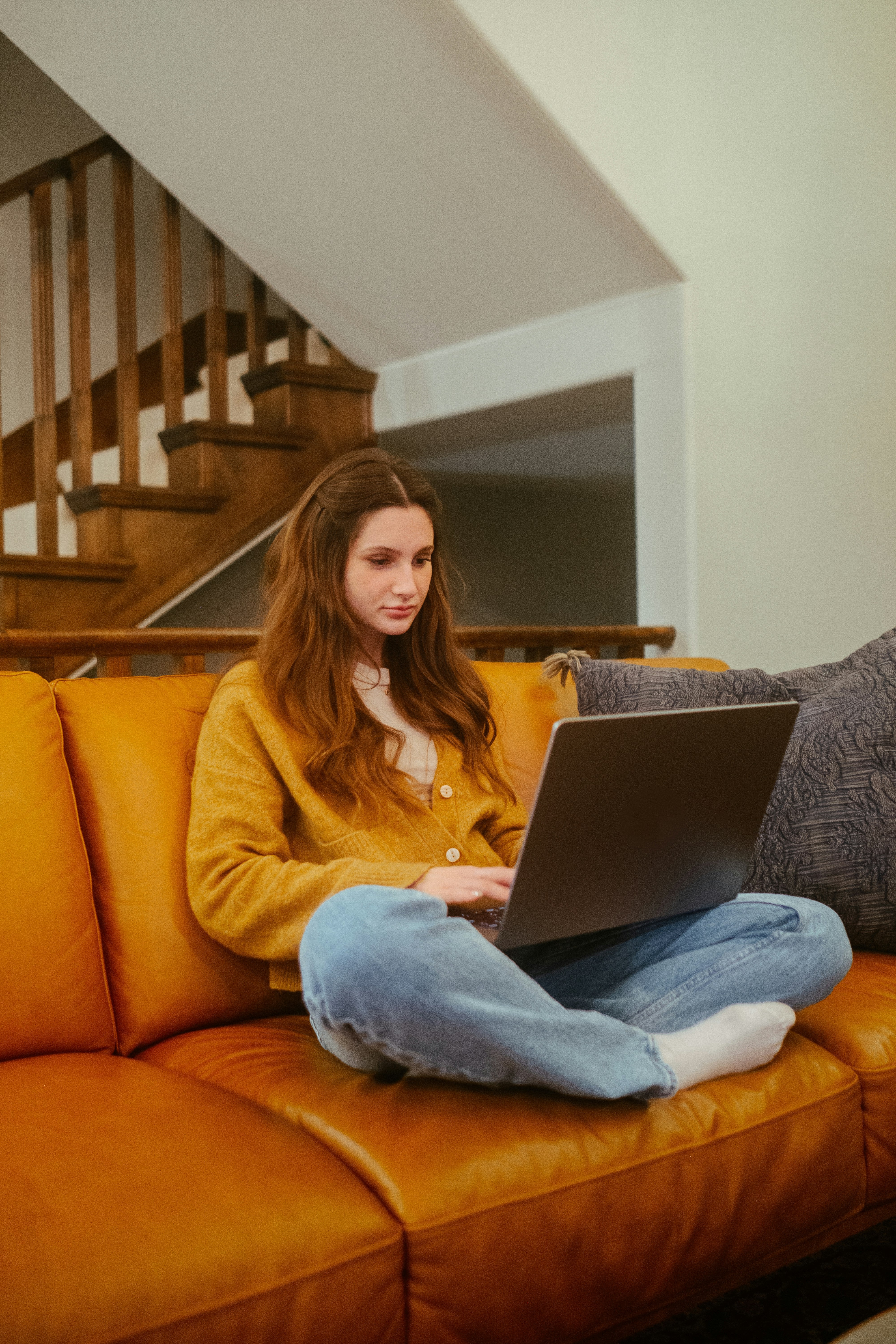 Woman using a laptop on an orange couch in a home setting