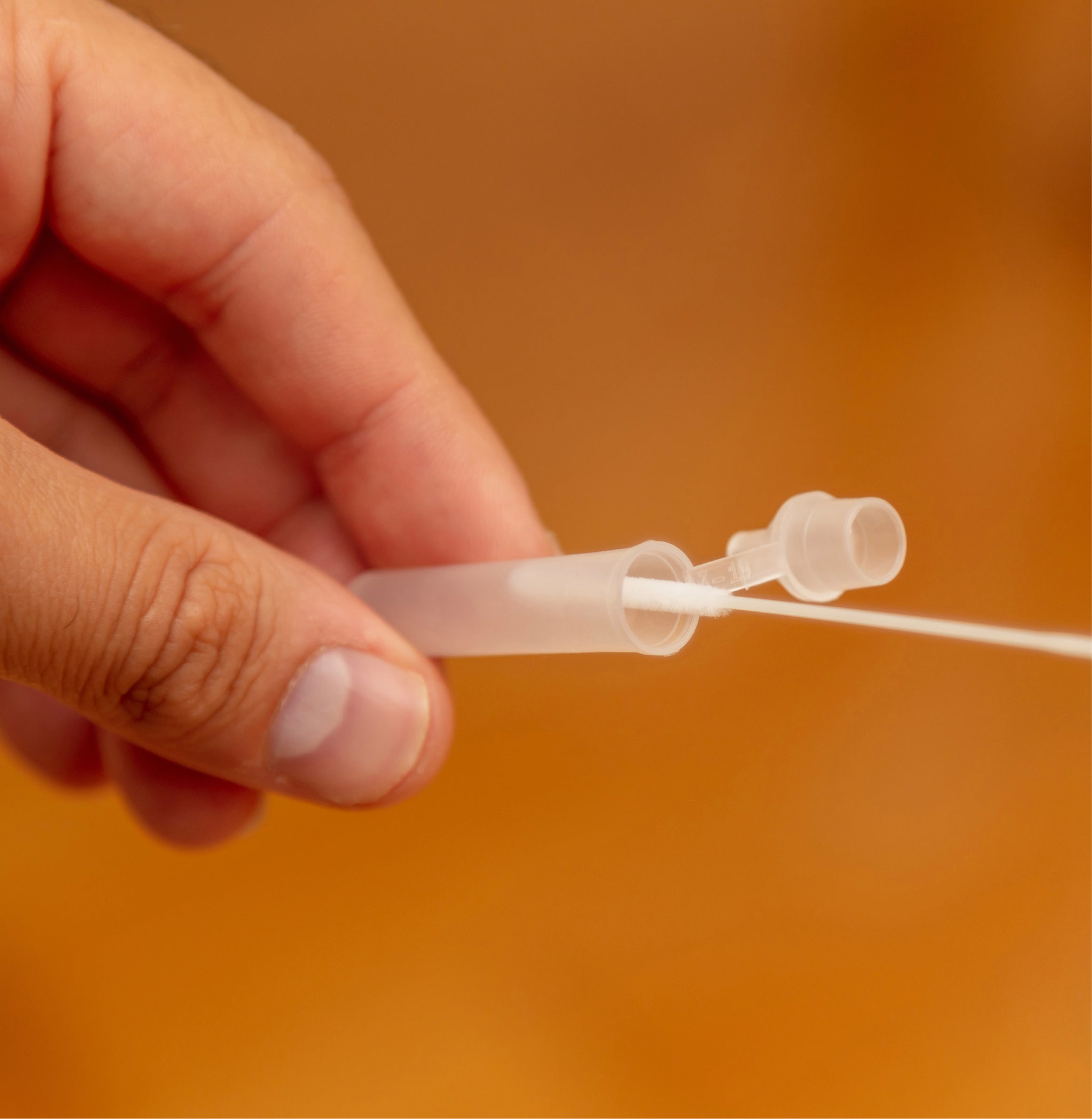 Hand holding a clear plastic tube against an orange background
