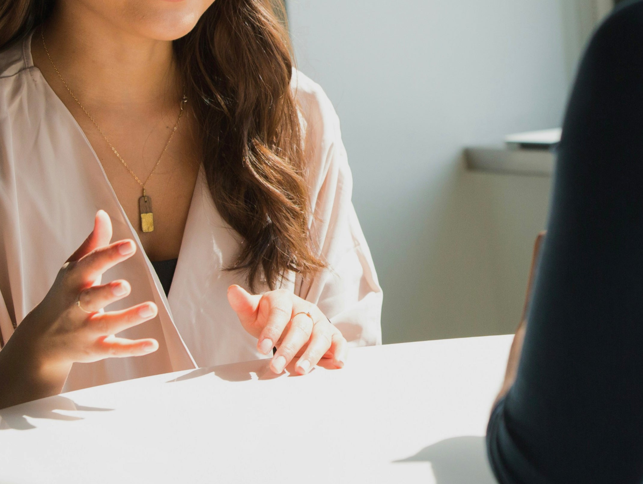 Woman in a white shirt sitting at a table with another person, engaged in conversation.
