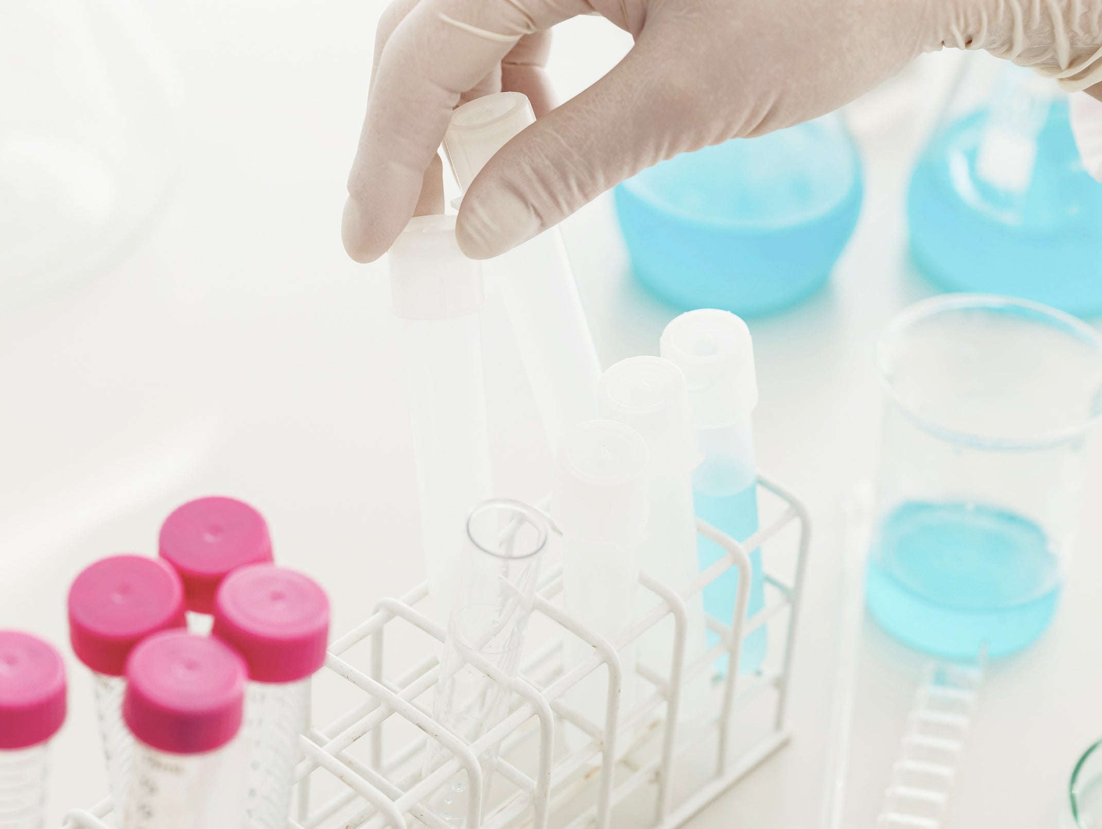 Hand in a glove selecting a blue container from a rack with pink lids on a white background