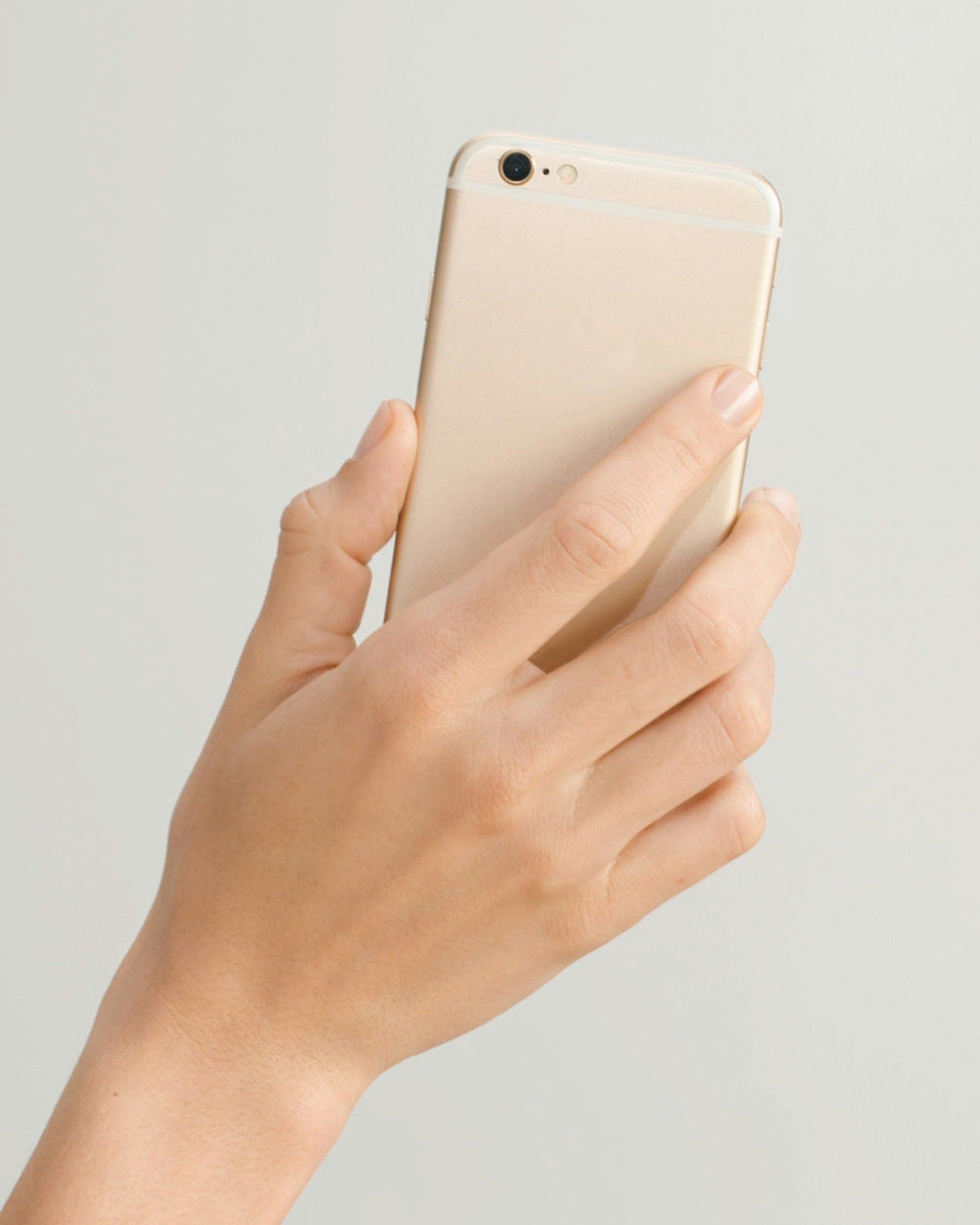 Hand holding a gold smartphone against a light gray background