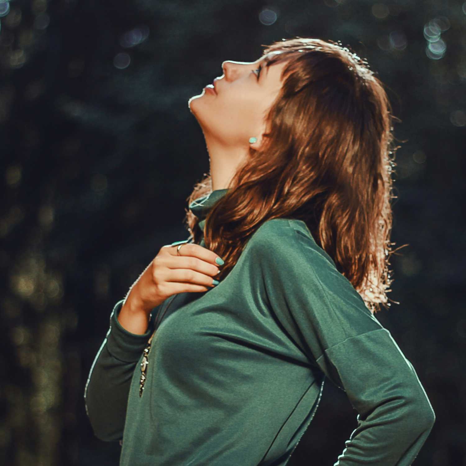 Woman in a green sweater looking up with a blurred natural background