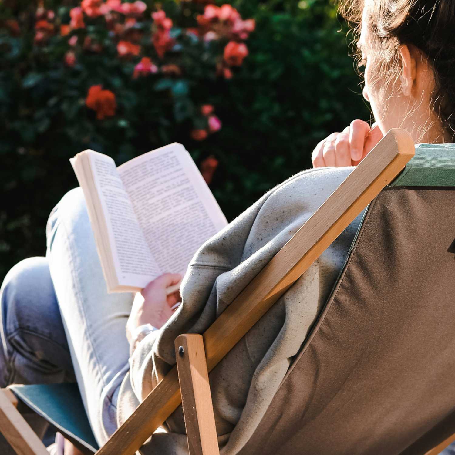 Person reading a book in a chair outdoors with greenery in the background